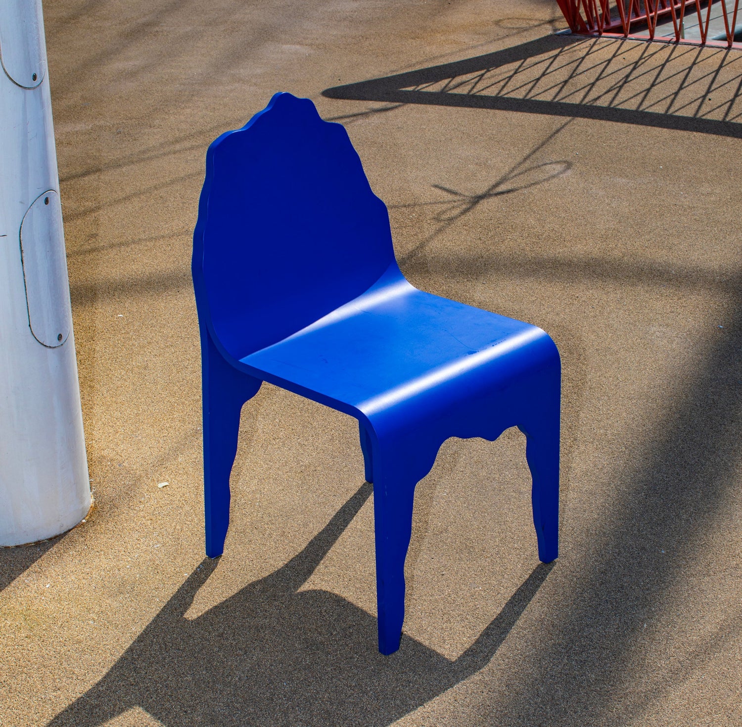 Blue LIEKSA chair on a concrete surface with a red metal structure in the background