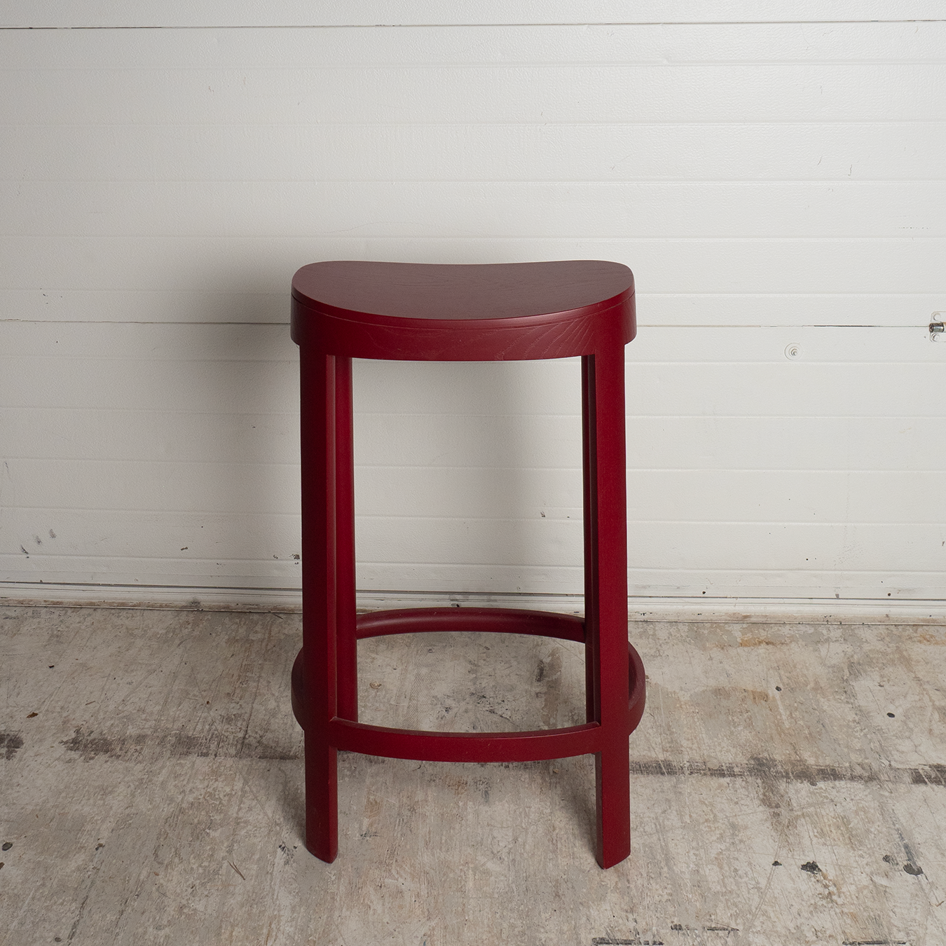 Red bar stool against a white wall on a concrete floor