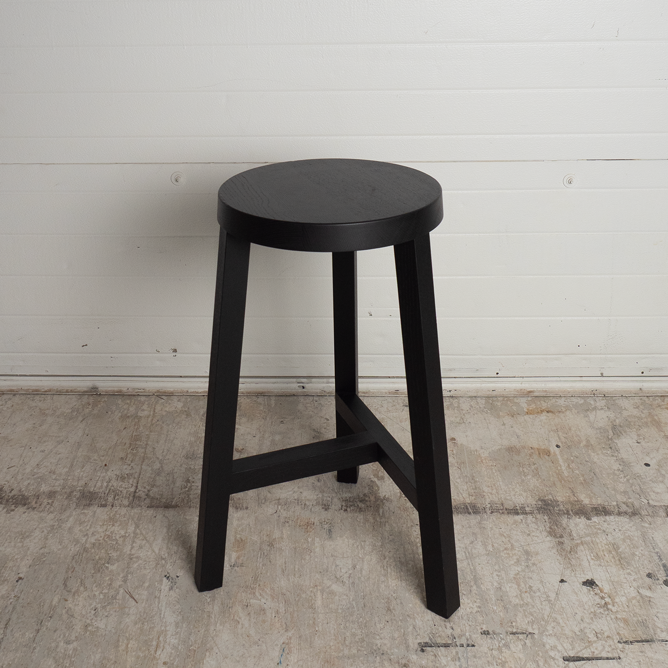 Black bar stool against a white wall on a concrete floor