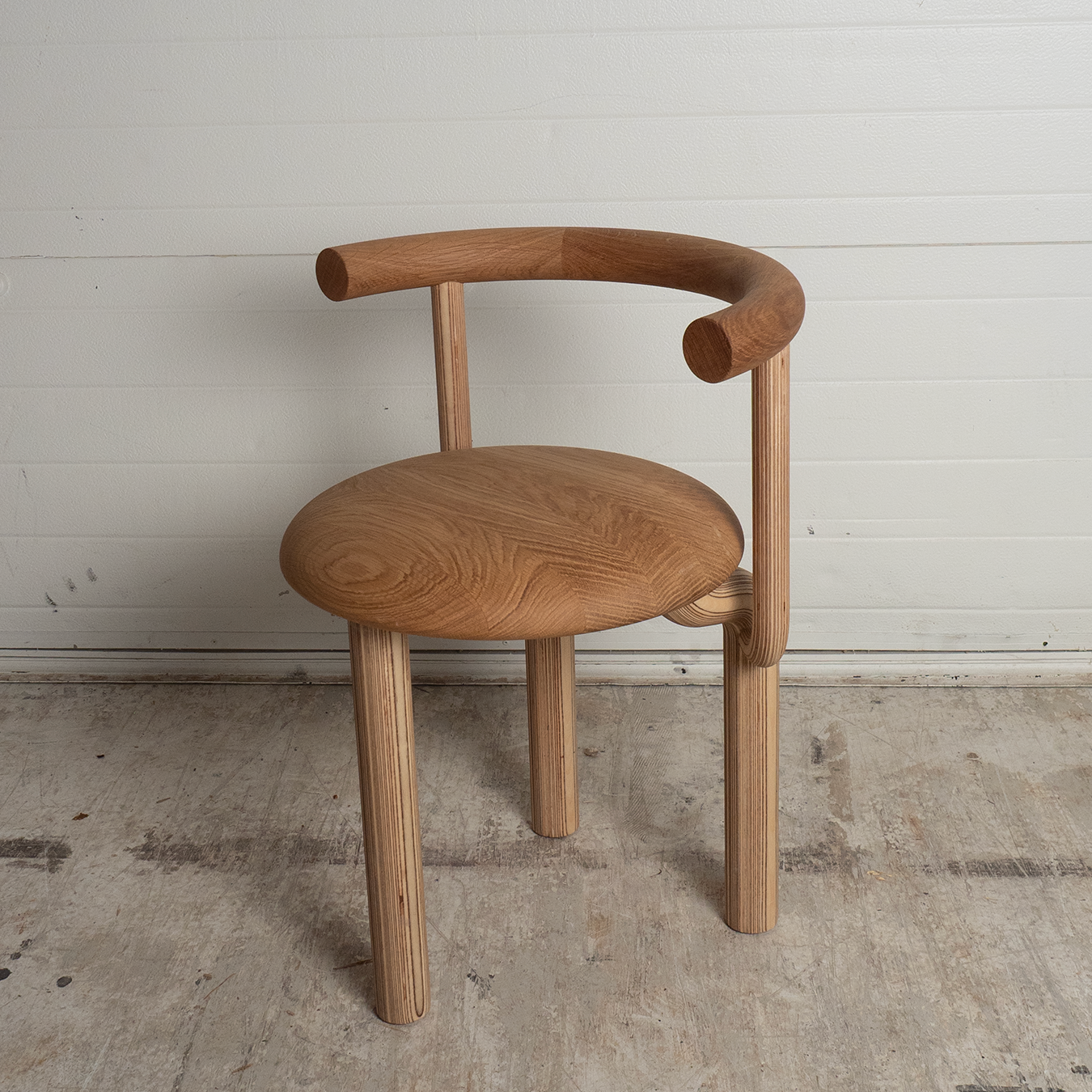 Wooden chair with curved armrests on a concrete floor against a white wall.